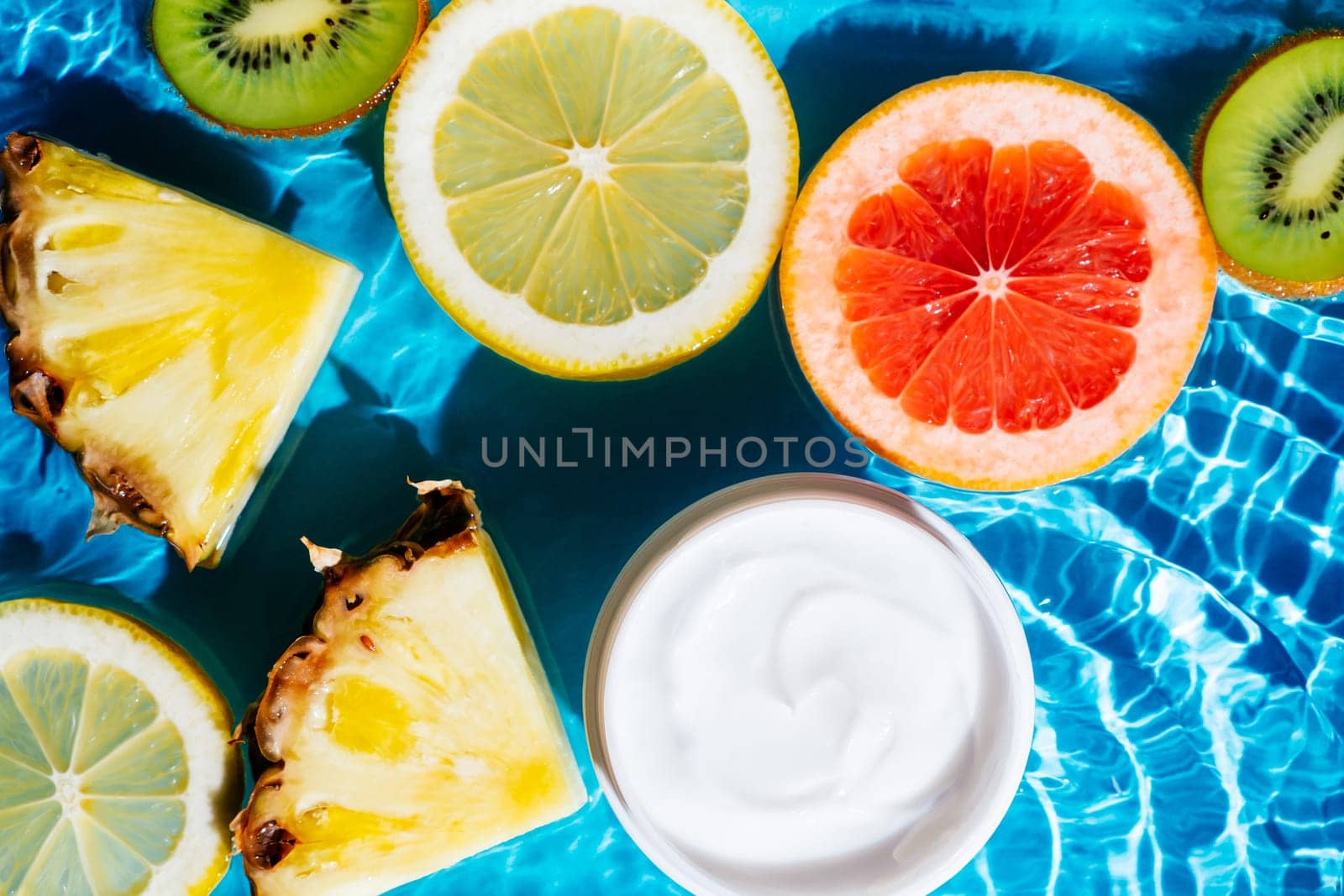 Facial jar cream milky beauty product in fruit citrus lemon, kiwi, orange, pineapple in water splashing fresh transparent, flecks. Flat lay, top view. Summer beach tropical. Skin care in summer
