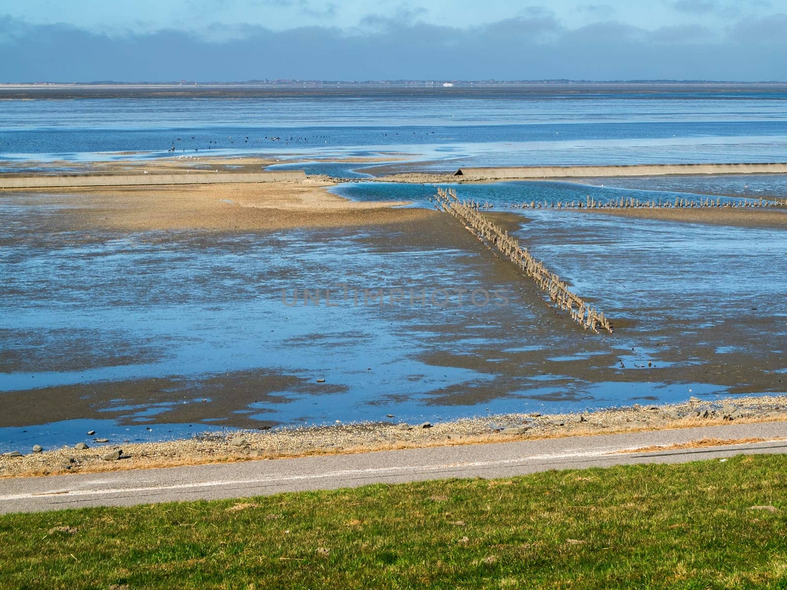 View from the dyke of the Lower Saxony Wadden Sea with the water draining away and a wide view to the island of Langeoog under a cloudy sky.