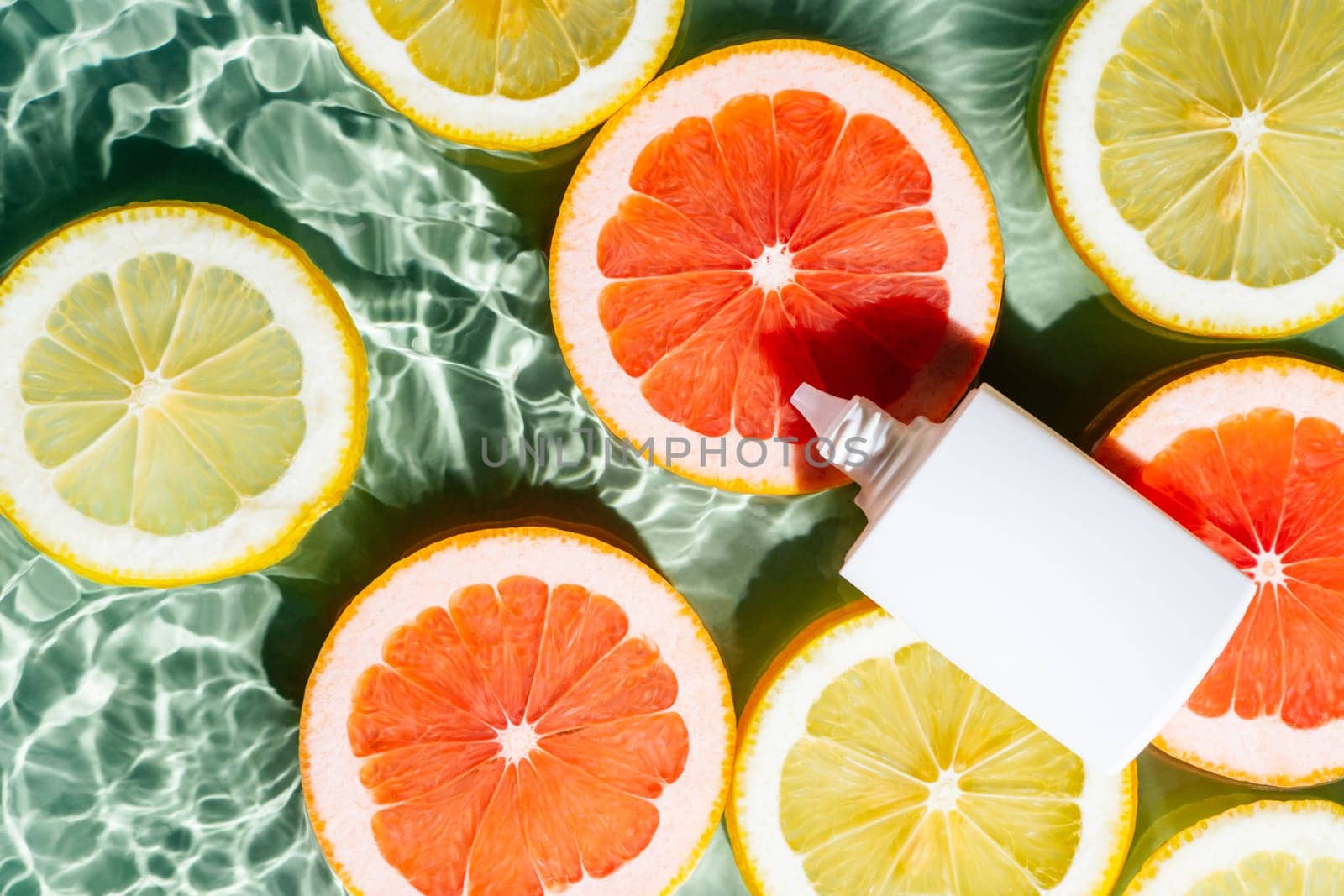White beauty product sunscreen cream vial tube bottle in transparent fresh exhilarant wave water with flecks, lemon and grapefruit citrus slices. Body skin care protection in summer travel. Flat lay.