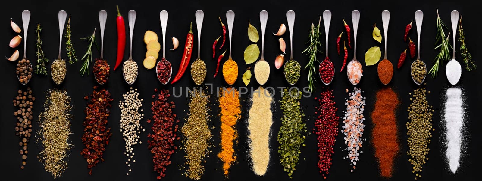 Various seasonings and herbs in spoons on dark background