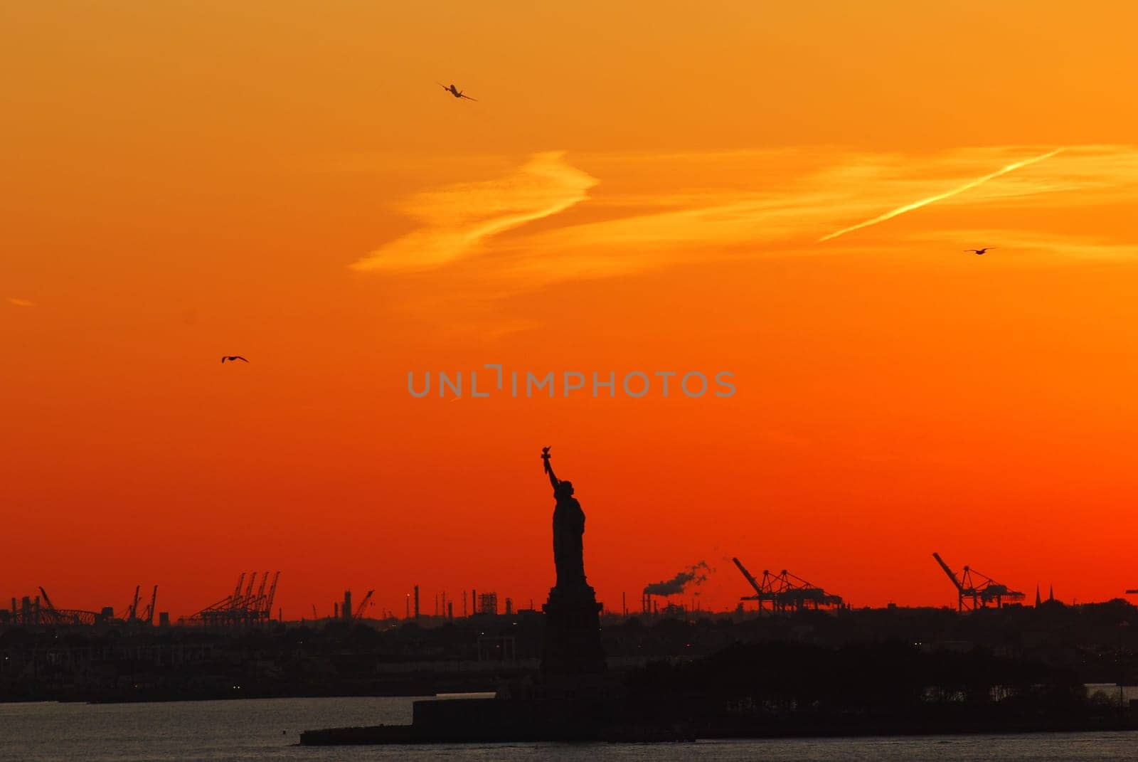 Silhouette of Statue of Liberty and Liberty Island in New York against an orange sunset sky
