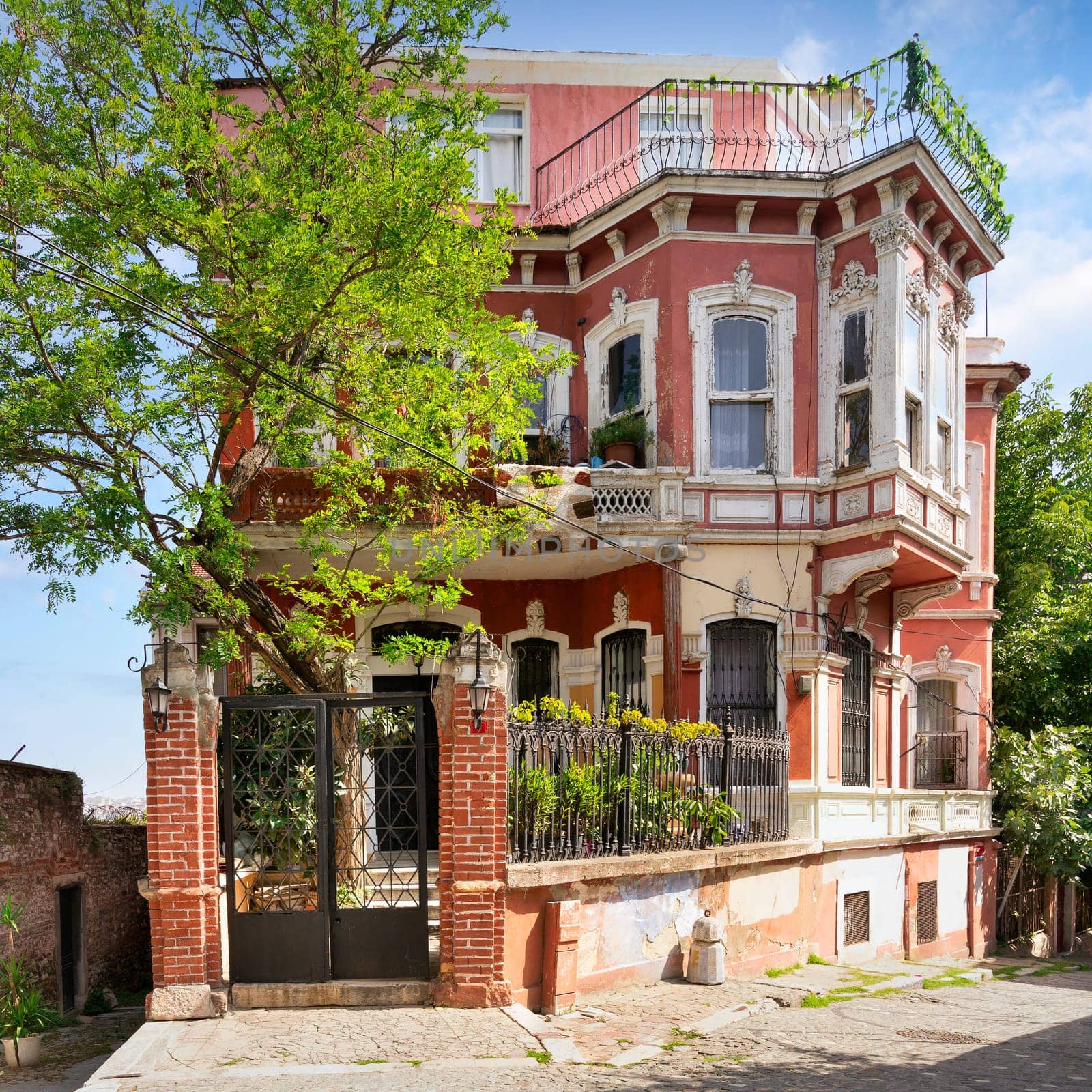 Exterior facade of old red residential building, with wrought iron windows, balconies, and green trees, Balat district, Istanbul, Turkey