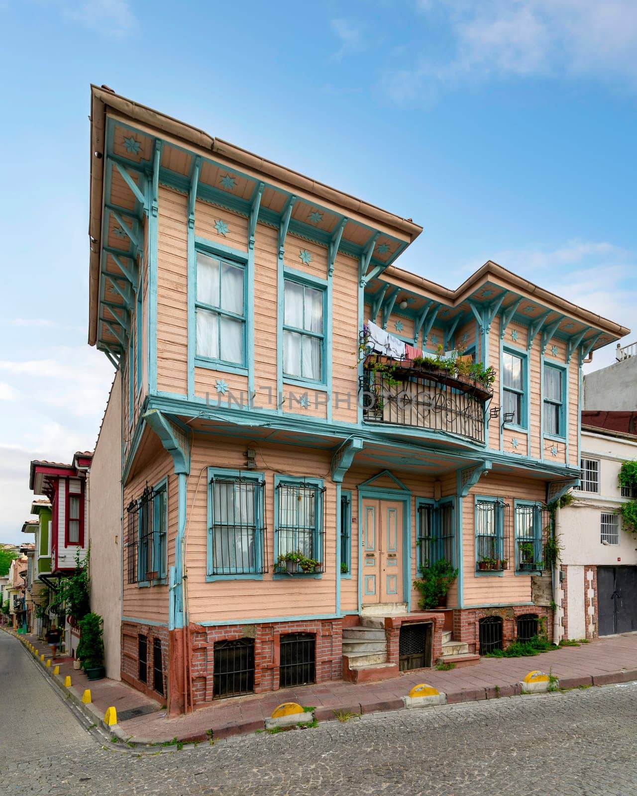 Exterior facade of old colorful wooden residential building with door, wrought iron windows, balcony, and green climber plants, Fatih district, Istanbul, Turkey