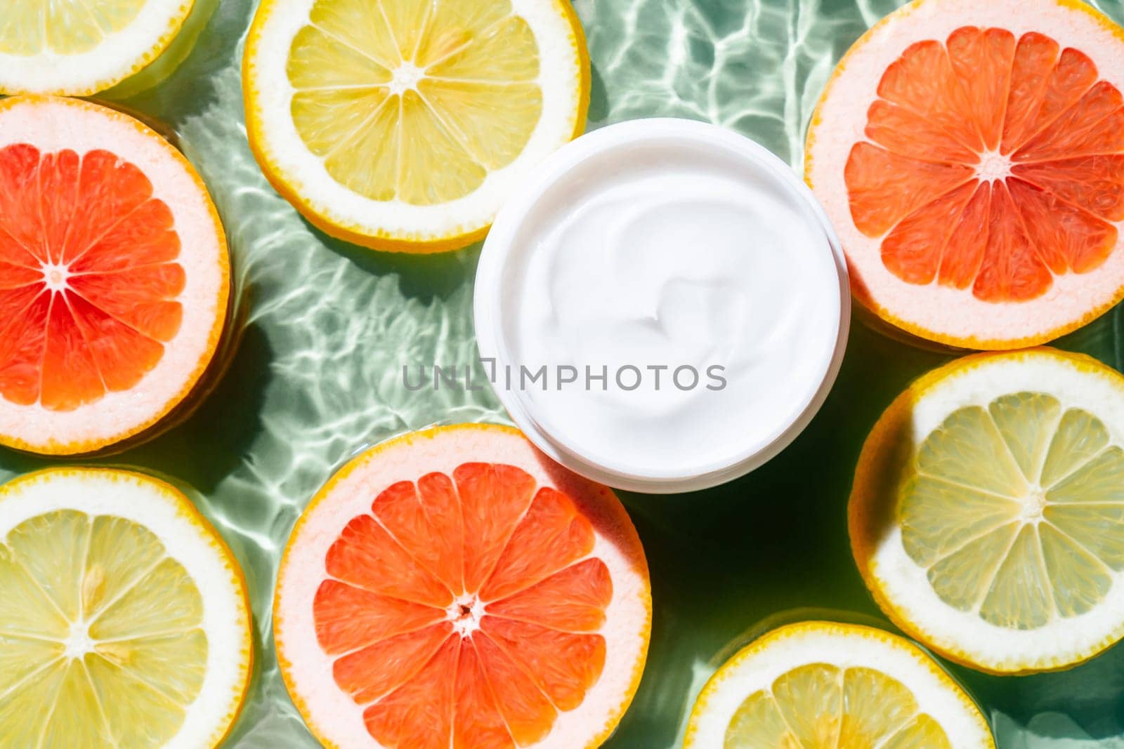 Facial jar cream milky beauty product with fruit citrus lemon and grapefruit slices in water splashing fresh transparent, flecks. Flat lay, top view. Summer beach tropical. Skin care in summer
