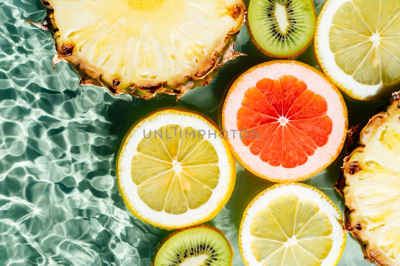 Colorful abstract image fruit citrus lemon, kiwi, orange, pineapple, grapefruit, lemon, pomelo water splashing fresh transparent surface, flecks. Flat lay, top view. Copy space. Summer beach tropical