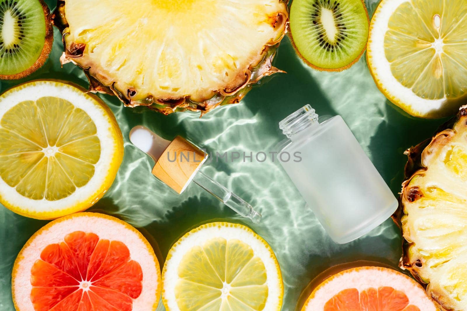 Facial pipette serum, whey beauty product near fruit citrus lemon, kiwi, orange, pineapple, grapefruit in water fresh transparent. Flat lay, top view. Organic skin body care in hot climate