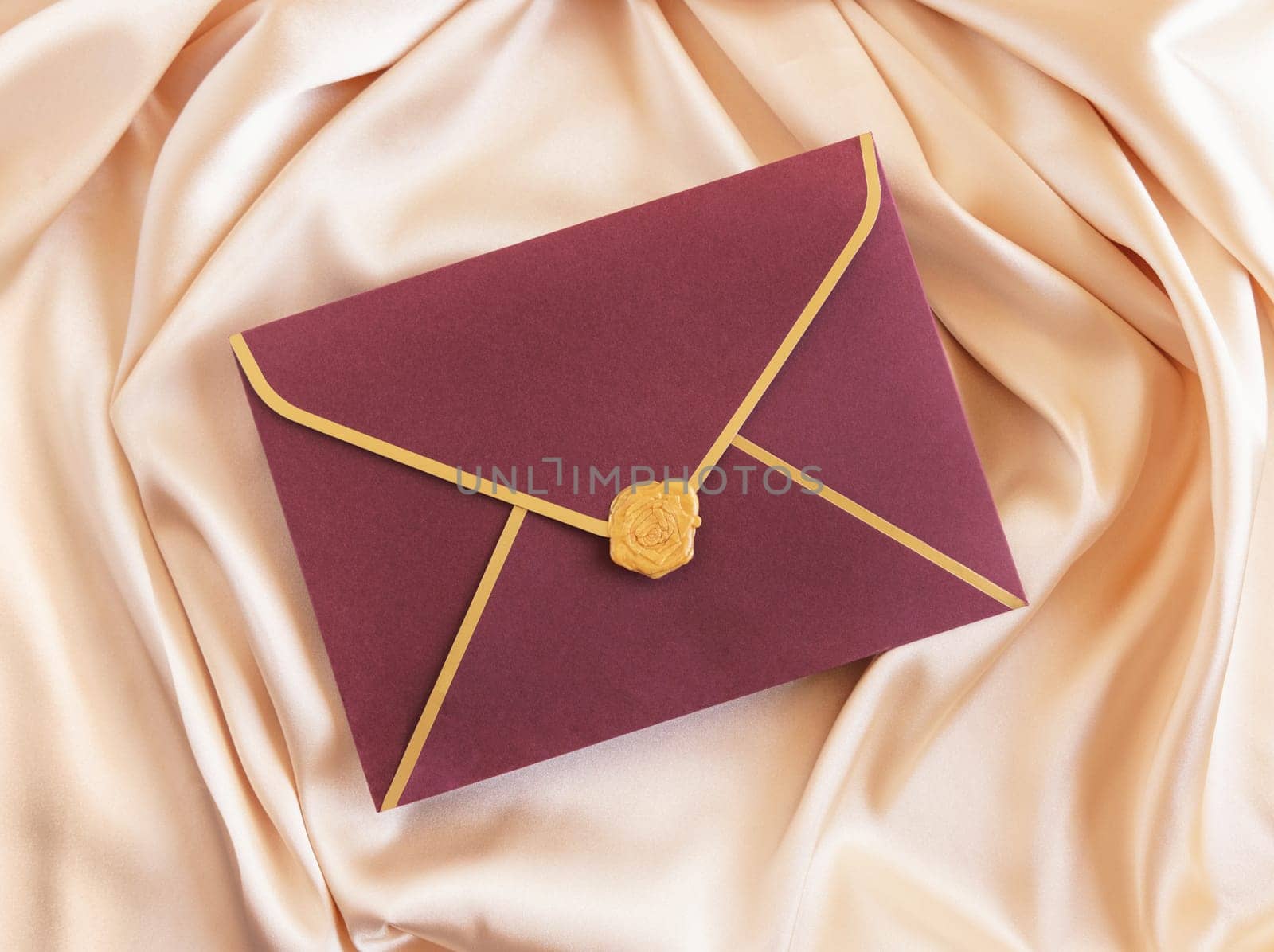 Red sealed envelope card on beige silky fabric drapery top view, mockup. Romantic scene with envelope, greeting or wedding Invitation. .