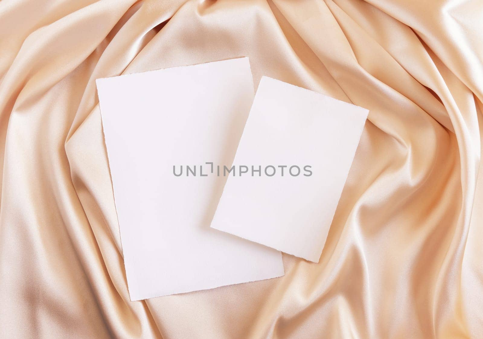 Blank cards on beige silky fabric drapery top view, mockup. Romantic scene with vertical paper cards, greeting or wedding Invitation. .