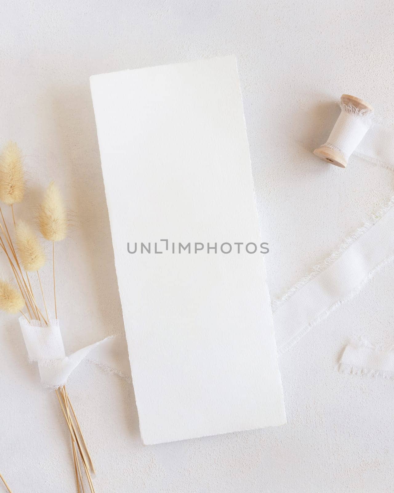 Blank card near silk ribbons and dried hare's tail grass top view on white, mockup. Boho romantic scene with vertical card. Bohemian or close to nature greeting or wedding Invitation