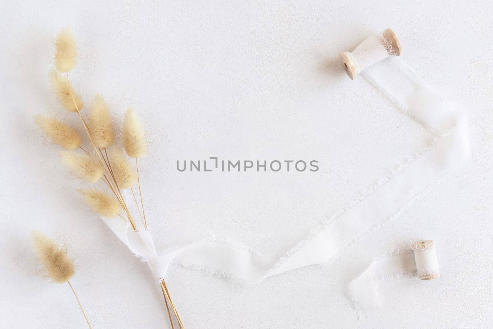 Hare's tail grass and silk ribbons with wooden bobbins on white top view, copy space. Romantic scene for wedding, valentines or mothers day cards