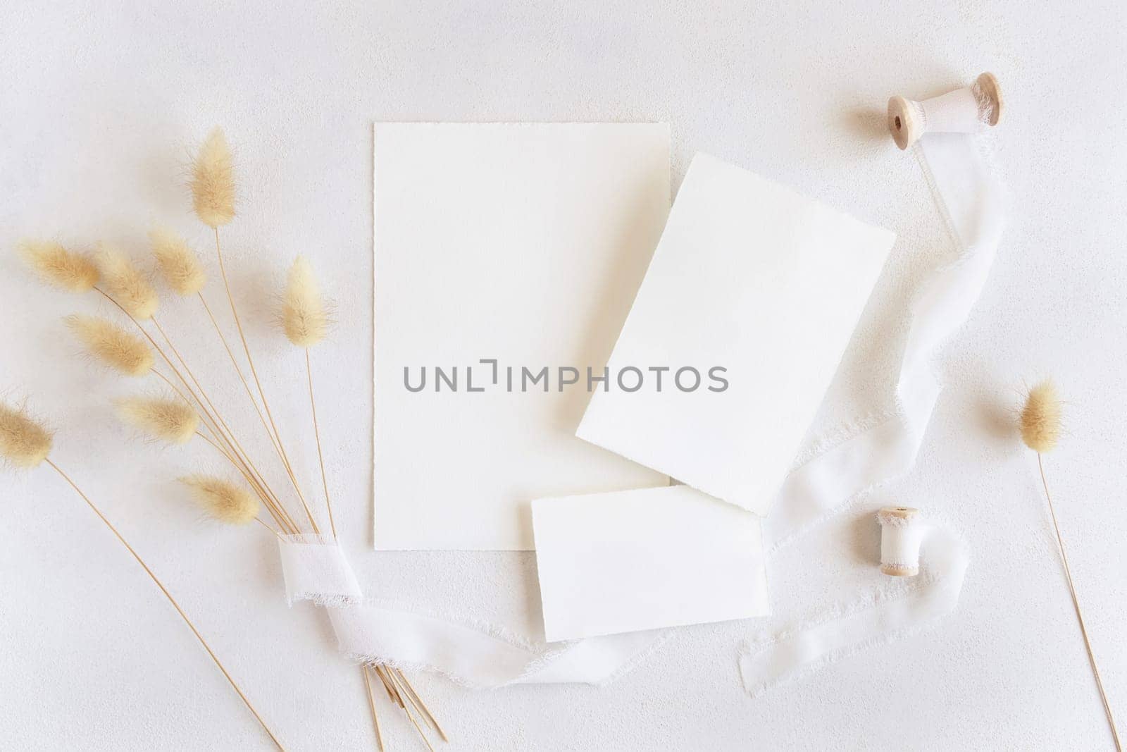 Blank cards near silk ribbons and dried hare's tail grass top view on white, mockup. Boho romantic scene with cards. Bohemian or close to nature greeting or wedding Invitation