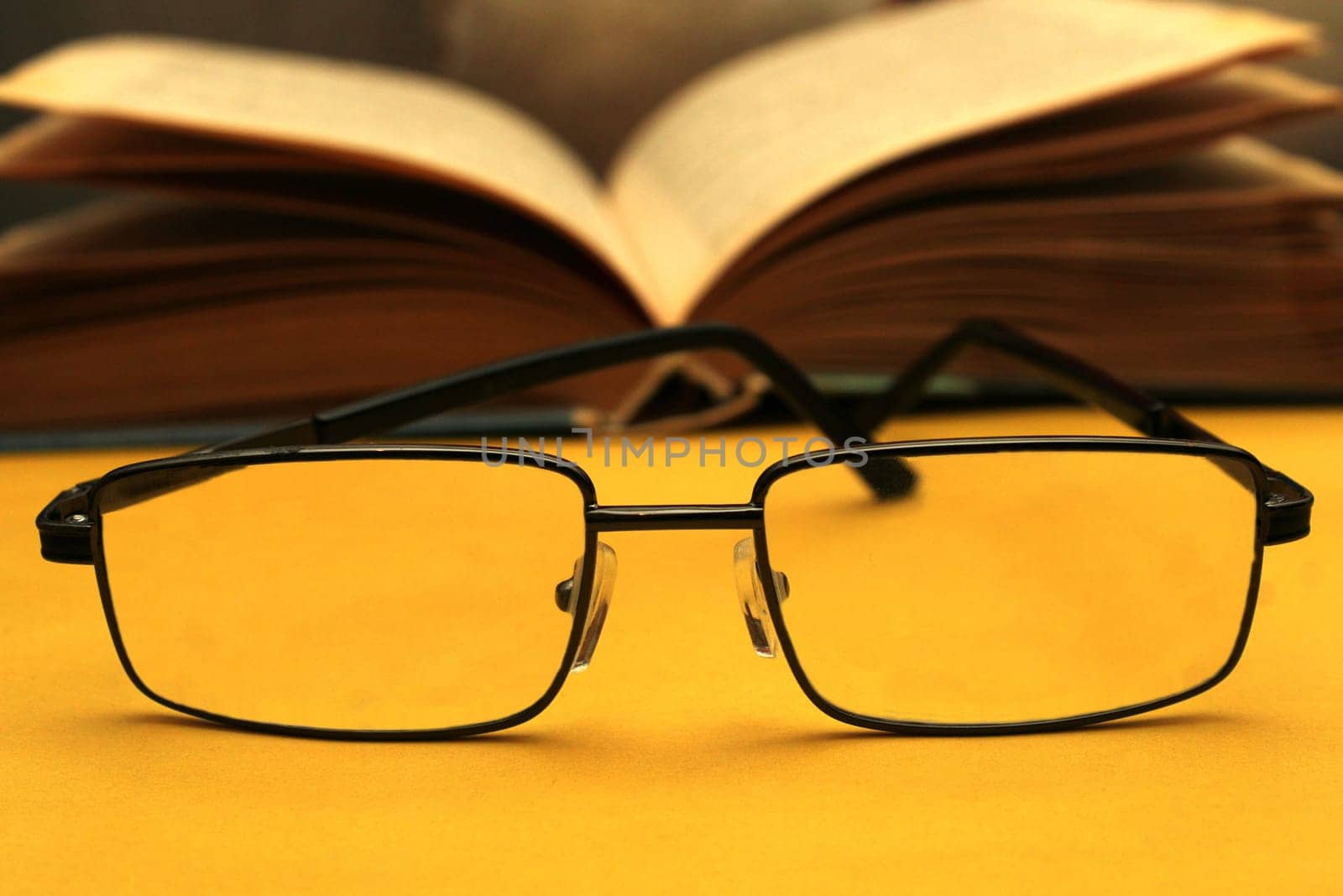 Glasses in a black frame on a yellow background. In the background is an open book. World Day of Sight.