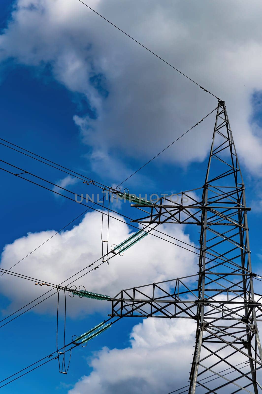 High-voltage power transmission tower with wires. High voltage line. Energy industry. Energy transfer. Blue sky. White clouds. Agricultural field. Cloudy horizon. Business. Electrician work.