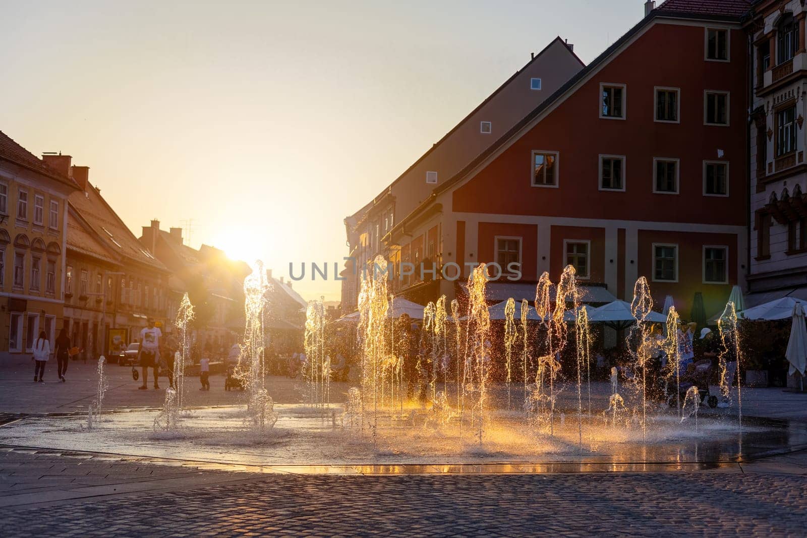 Flowing fountain in center of Maribor in golden hour. Splashing water on square in old city in Slovenia in sunset light. Historical building in turistic town.