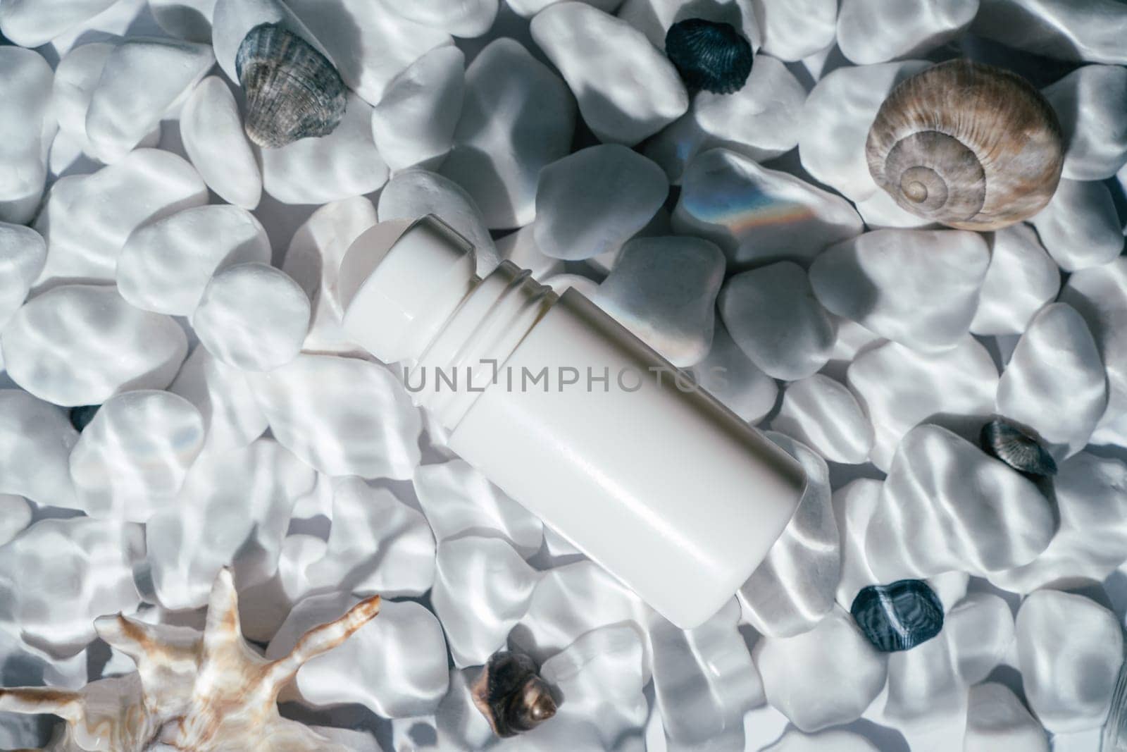 White beauty product roll on antiperspirant deodorant anti sweat smell, vial in transparent fresh water with flecks and waves above bottom of white stones and shell. Skin care protection. Flat lay.
