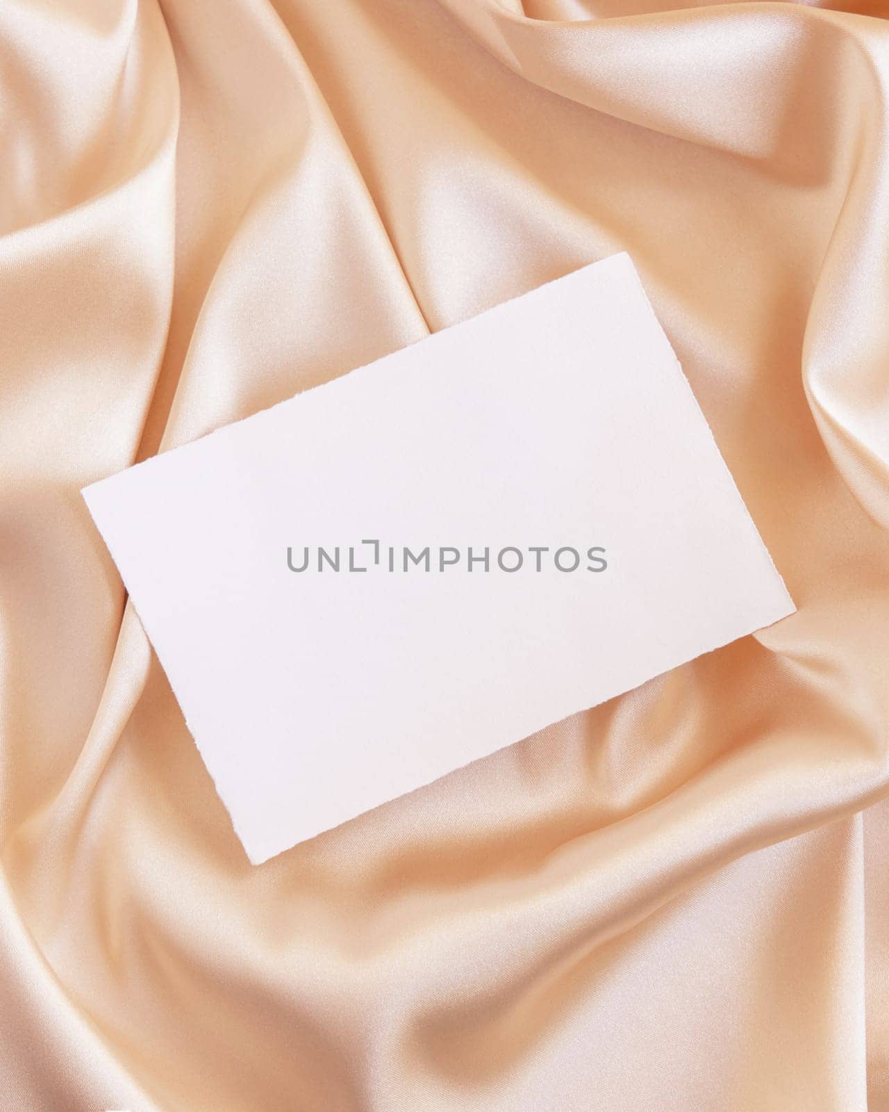 Blank card on beige silky fabric drapery top view, mockup. Romantic scene with horizontal paper card, greeting or wedding Invitation. .