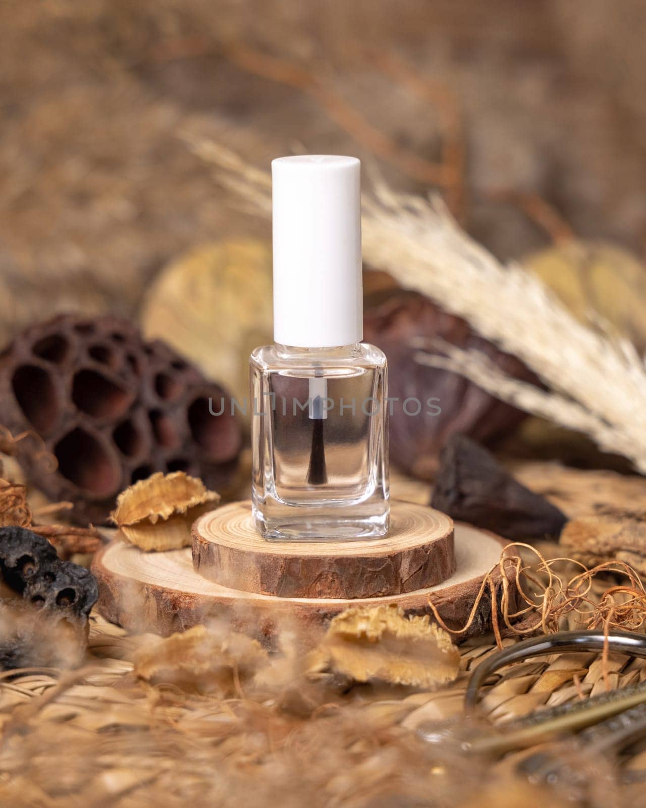 Refillable Bottle with Brush Cap on wood near natural boho decorations close up. Eco friendly Skincare or nail product. Bohemian composition with dried leaves and flowers.