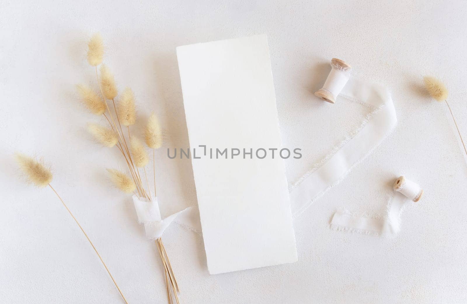 Blank cards near silk ribbons and dried hare's tail grass top view on white, mockup. Boho romantic scene with vertical card. Bohemian or close to nature greeting or wedding Invitation