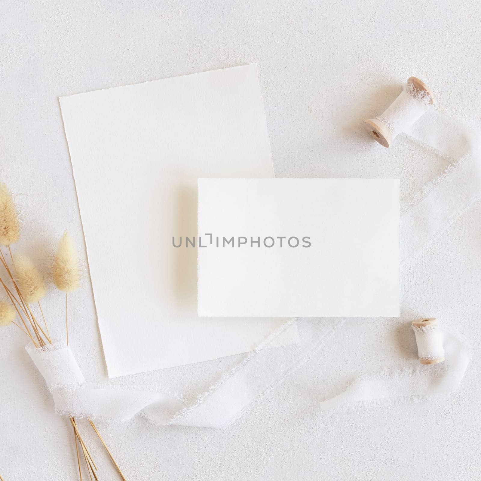 Blank cards near silk ribbons and dried hare's tail grass top view on white, mockup. Boho romantic scene with vertical cards. Bohemian or close to nature greeting or wedding Invitation