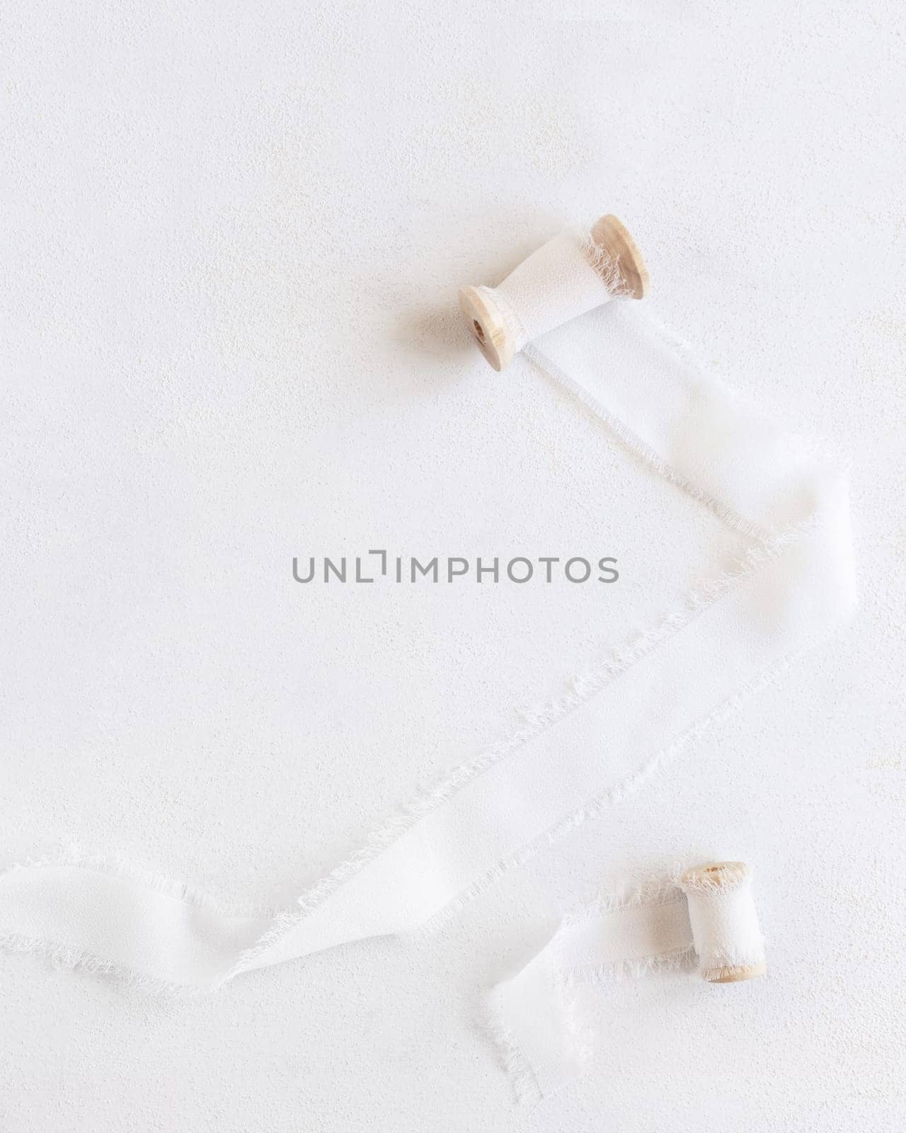 Silk ribbons with wooden bobbins on white top view, copy space. Romantic scene for wedding, valentines or mothers day cards