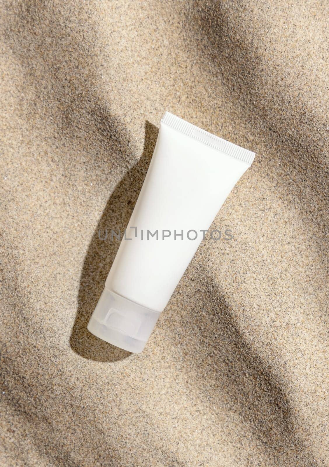 White cream tube on beige sand top view, hard light. Package mockup. Natural skincare or SPA product. Facial cosmetics for beauty routine. Zen style with waves on sand, minimal aesthetic