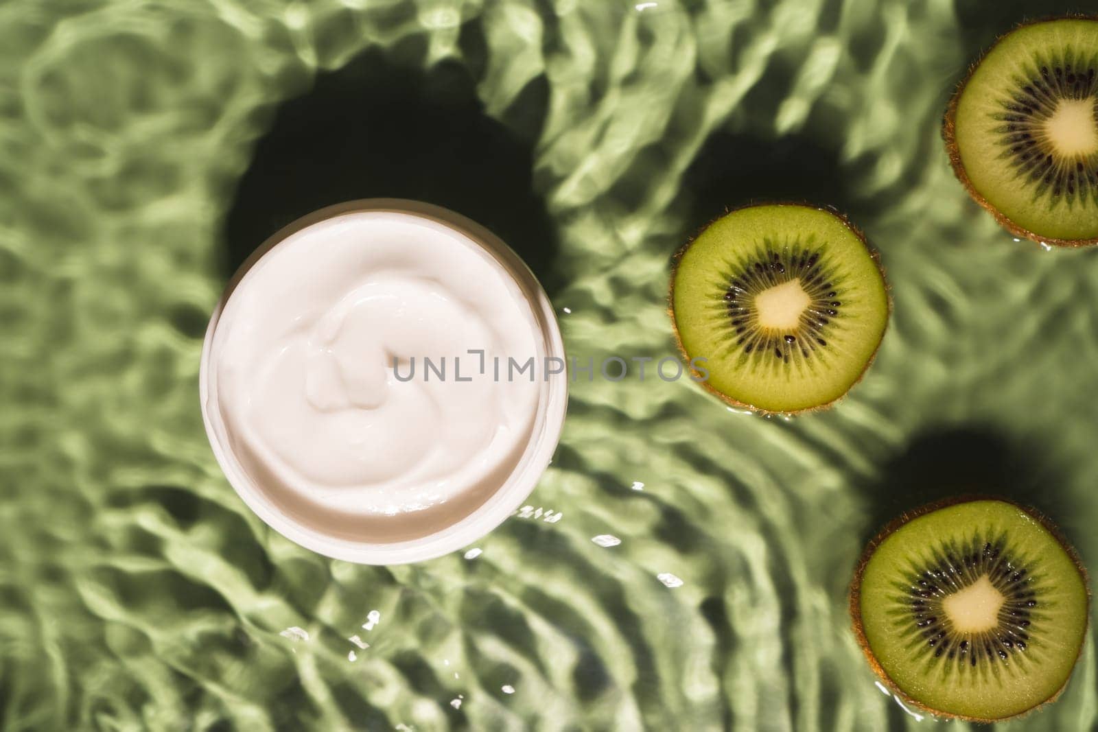 Facial jar cream milky beauty product with fruit tropical kiwi slices in green water splashing fresh transparent, flecks. Flat lay, top view. Summer beach tropical. Skin care in summer