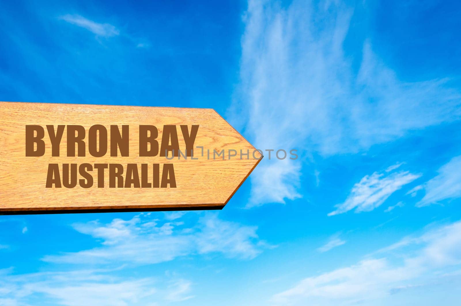 Wooden arrow sign pointing destination BYRON BAY, AUSTRALIA  against clear blue sky with copy space available. Travel destination concept  image