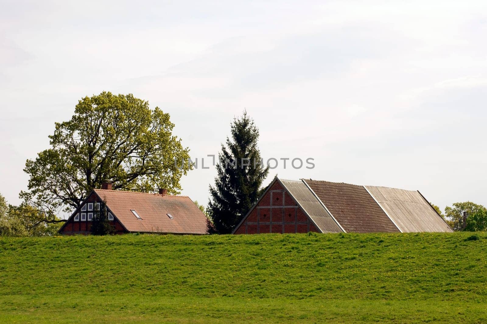 The roof of a barn and a house behind a green dike.