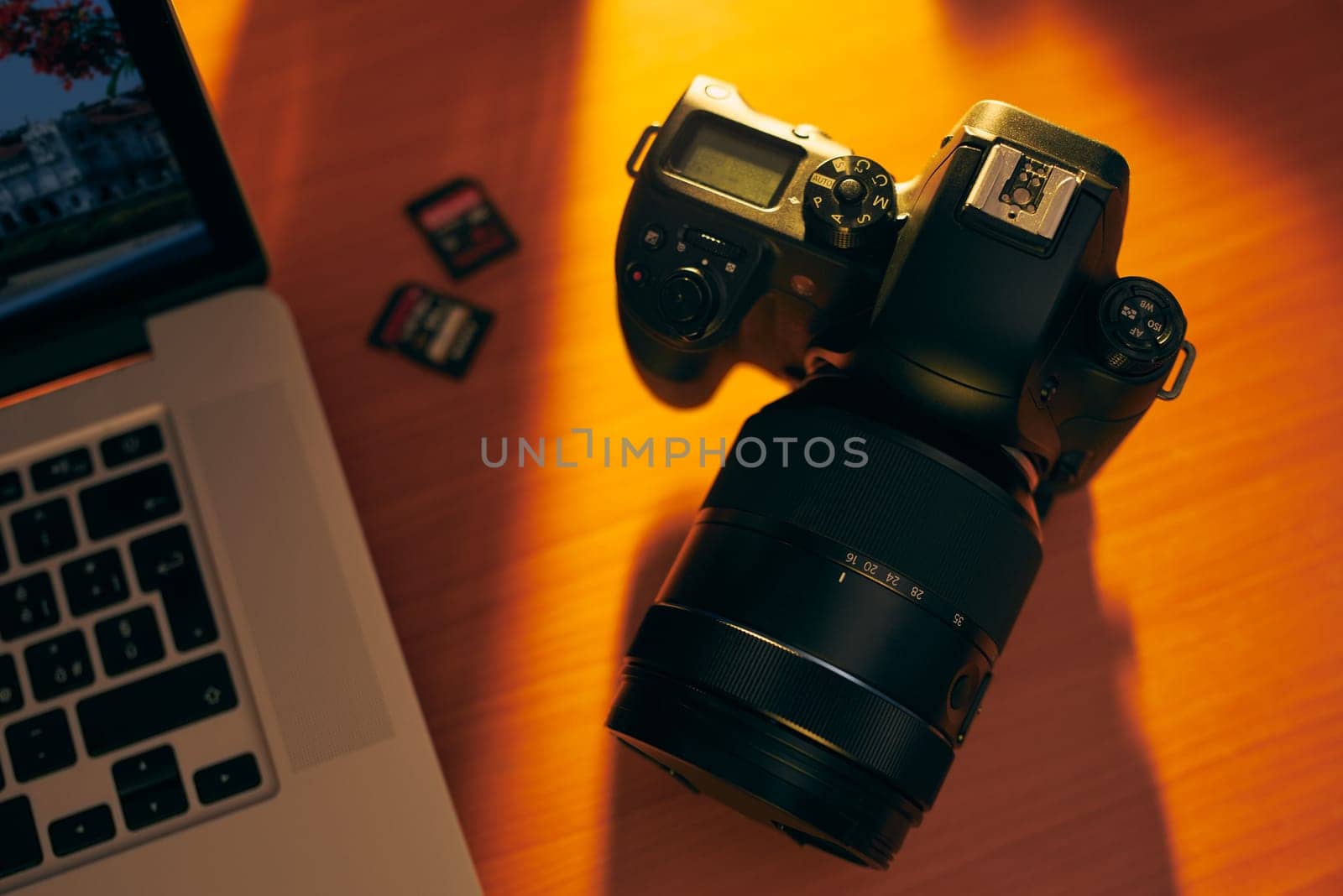Still life of dslr camera, sdhc flash memories and laptop computer on wooden table. High angle view of objects with sunset lighting