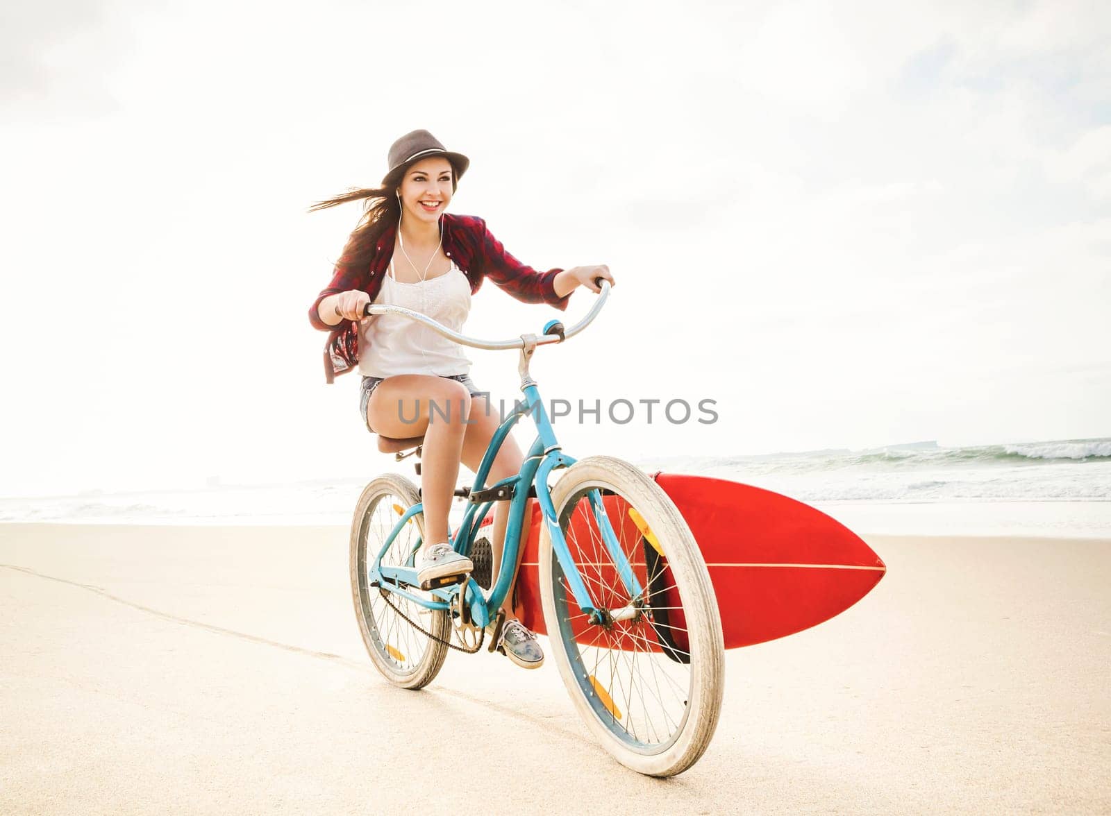 Surfer young woman riding her bicycle on the beach