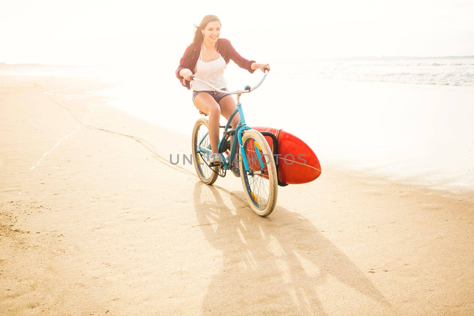 Surfer young woman riding her bicycle on the beach