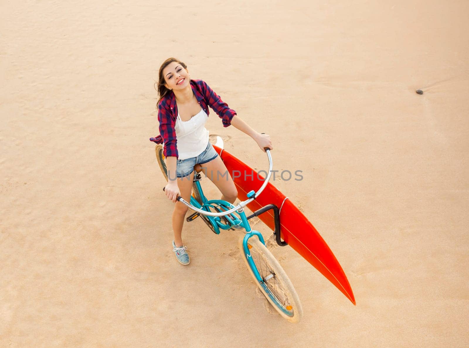 Surfer young woman riding her bicycle on the beach