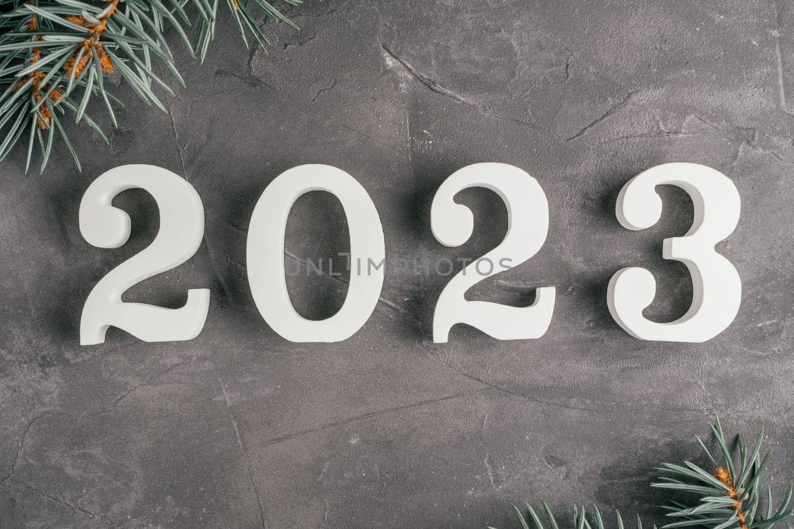 Happy New Year 2023. White wooden numbers 2023 lying on gray uneven concrete surface with Christmas tree branches. Merry Christmas. Top view