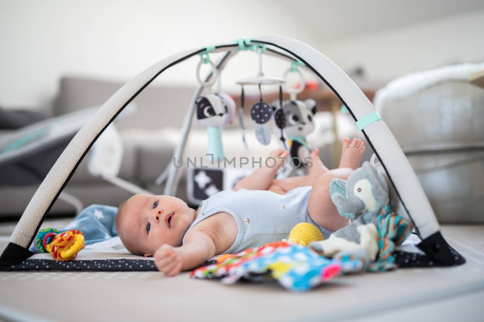 Cute baby boy playing with hanging toys arch on mat at home Baby activity and play center for early infant development. Baby playing at home.