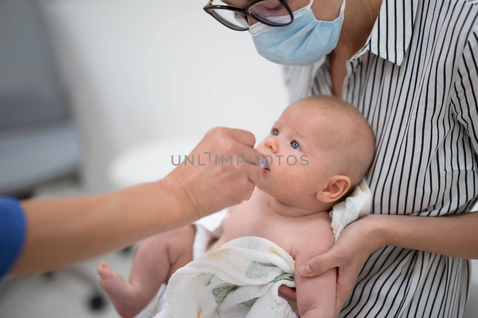 Pediatrician administring oral vaccination against rotavirus infection to little baby in presence of his mother. Children health care and disease prevention.