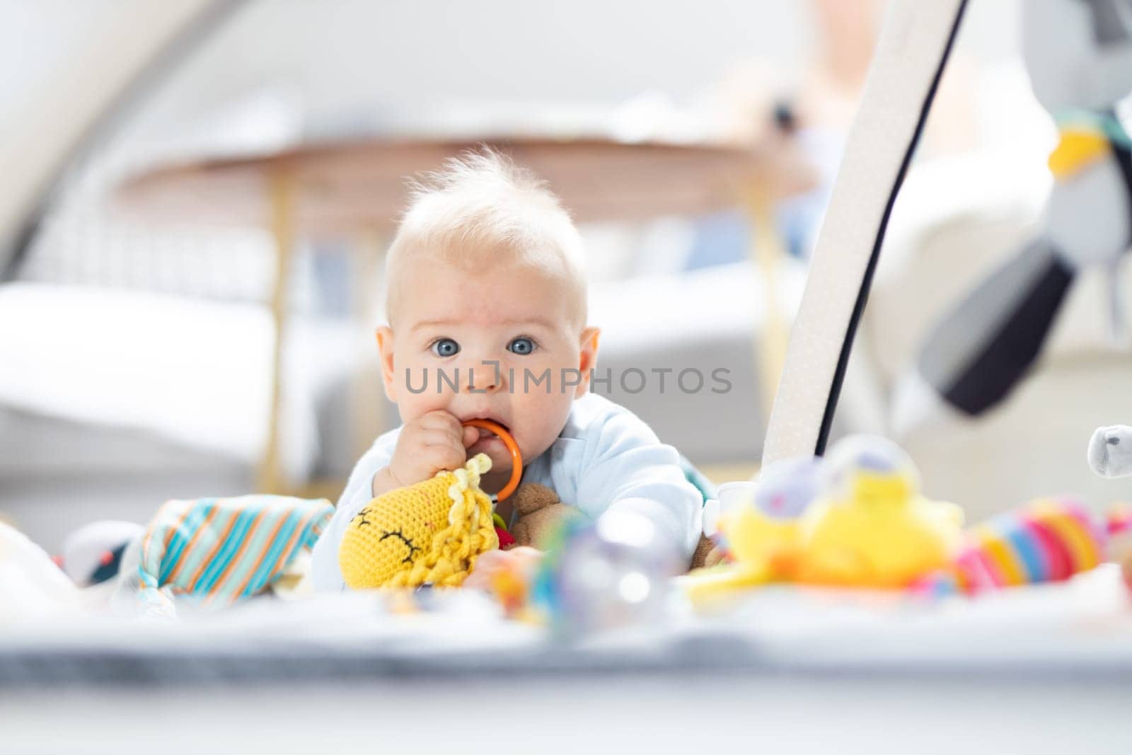 Cute baby boy playing with hanging toys arch on mat at home Baby activity and play center for early infant development. Baby playing at home.