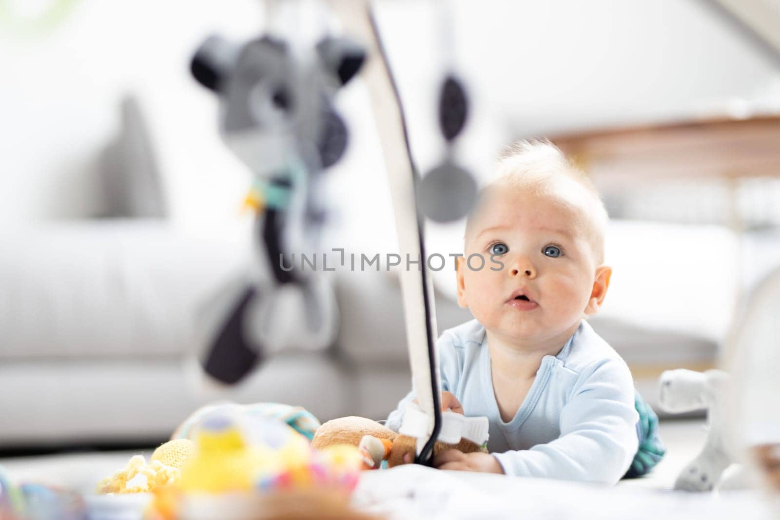 Cute baby boy playing with hanging toys arch on mat at home Baby activity and play center for early infant development. Baby playing at home.