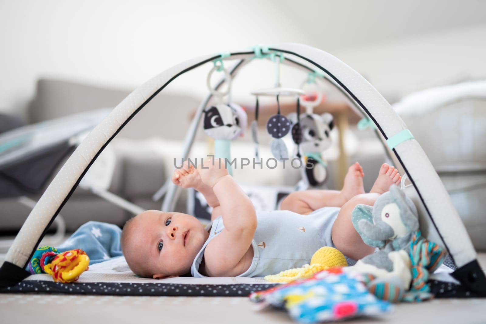 Cute baby boy playing with hanging toys arch on mat at home Baby activity and play center for early infant development. Baby playing at home.