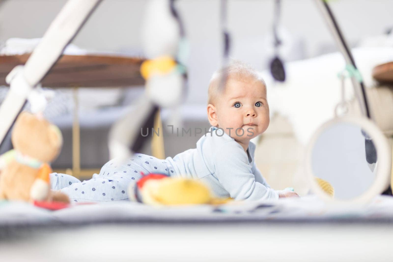 Cute baby boy playing with hanging toys arch on mat at home Baby activity and play center for early infant development. Baby playing at home.