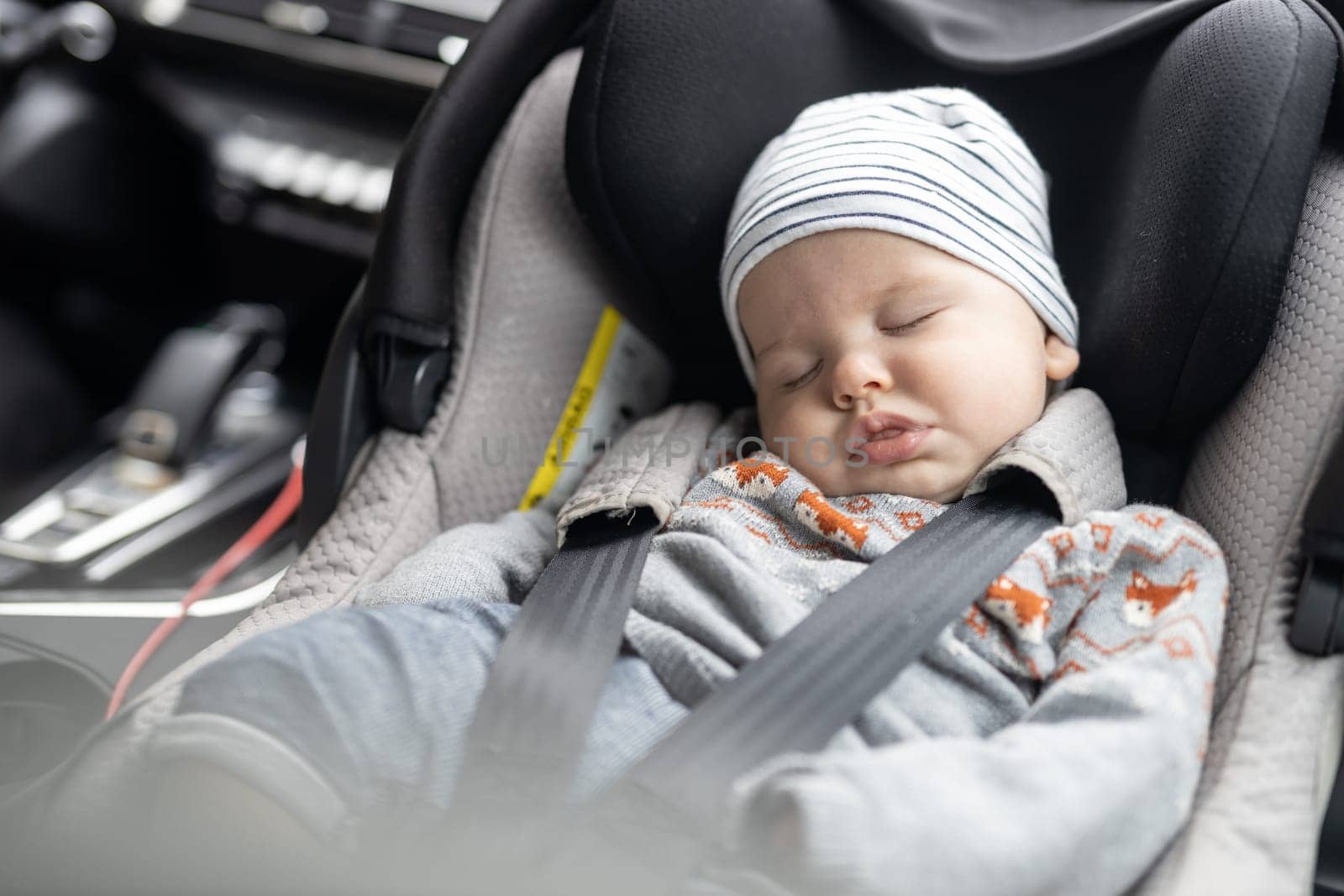 Cute little baby boy sleeping strapped into infant car seat in passenger compartment during car drive