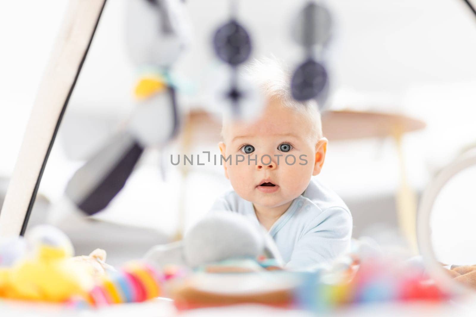 Cute baby boy playing with hanging toys arch on mat at home Baby activity and play center for early infant development. Baby playing at home.