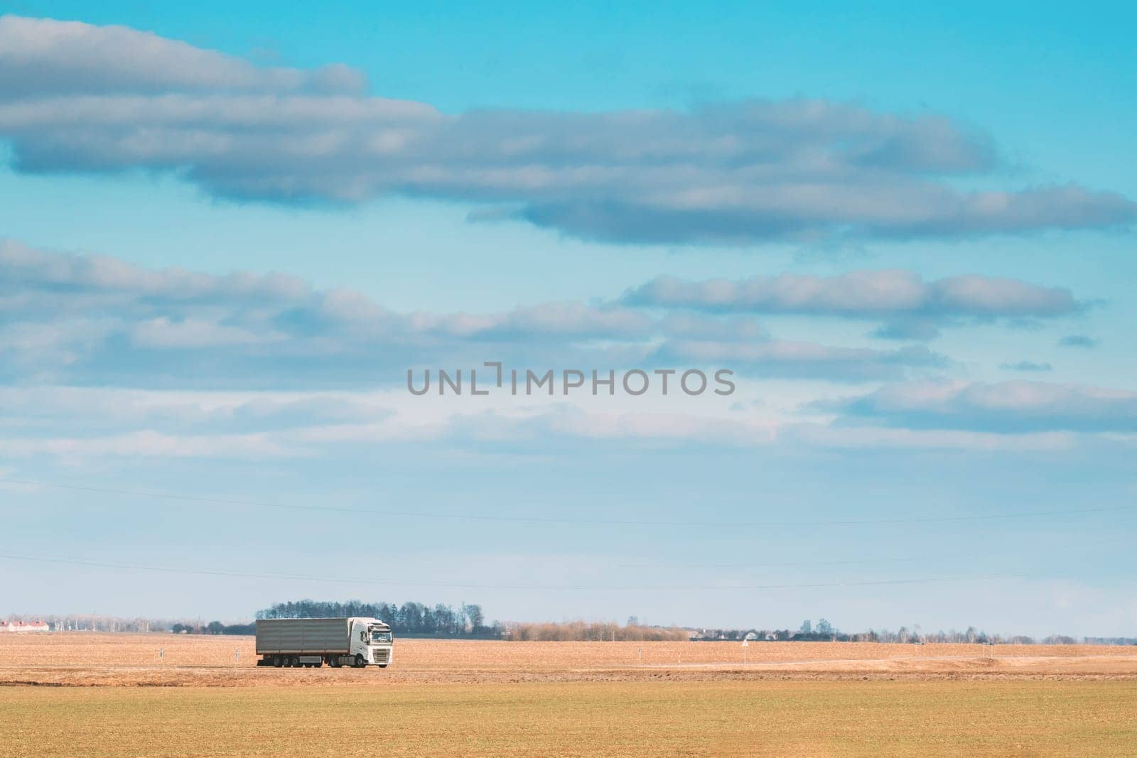 Truck Or Tractor Unit, Prime Mover, Traction Unit In Motion On Road, Freeway. Asphalt Motorway Highway Against Background Of Spring Meadow Field Landscape. Business Transportation And Trucking Industry