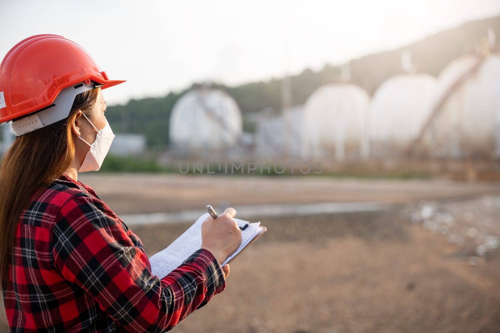 Petroleum Engineers. Happy Asian worker woman in oil chemical industry worker working visual inspection list on clipboard in plant, do Action of worker do safety checklist which is clipped
