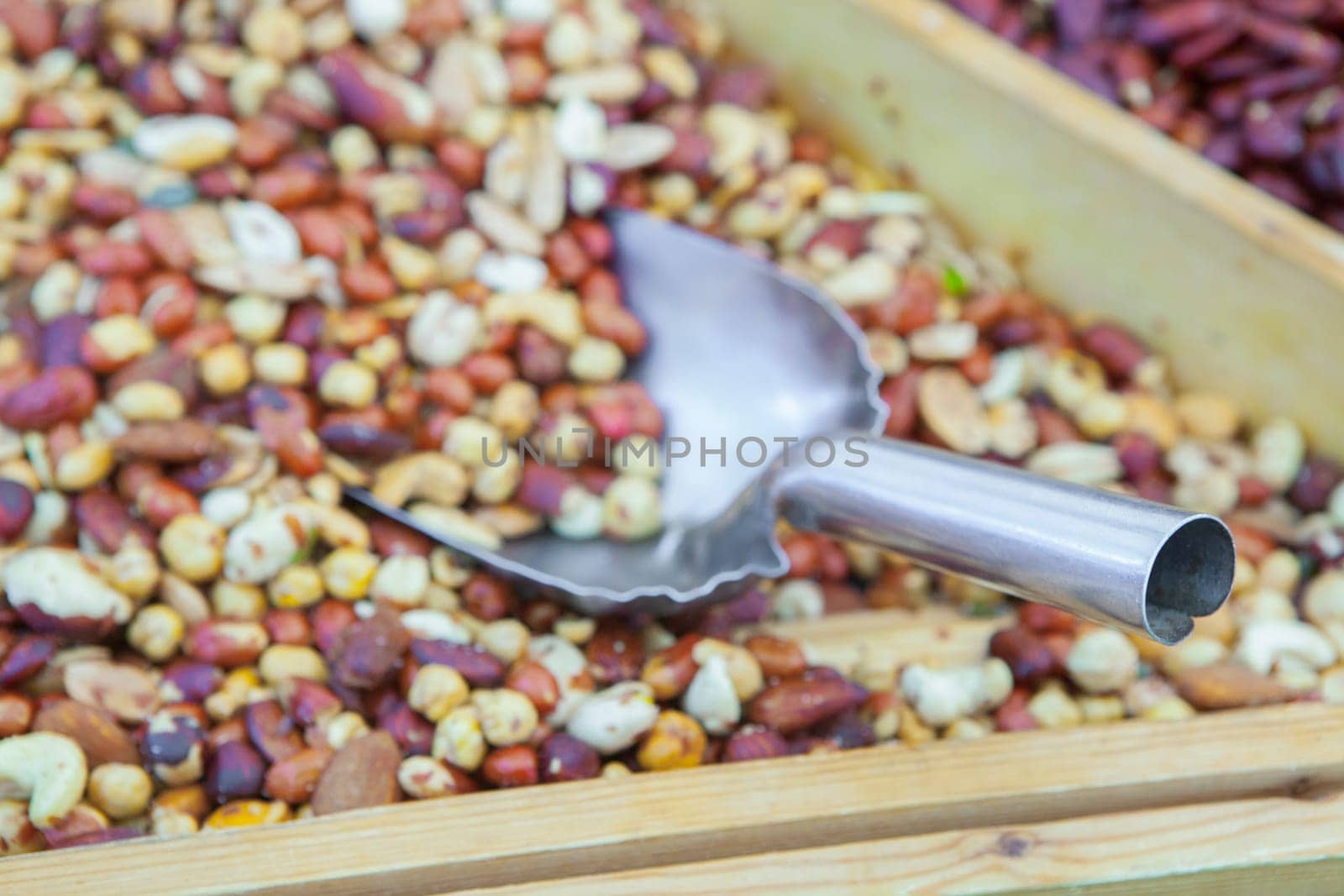 Wooden box with an assortment of fried salty dry fruits. Focus on shovel