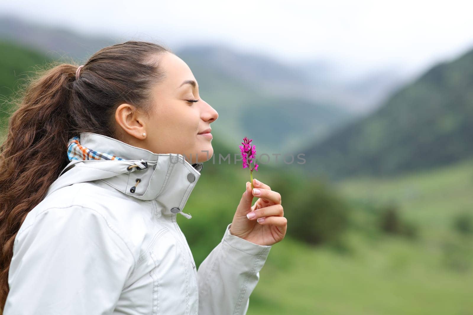 Side view portrait of a hiker smelling wild flower in the mountain