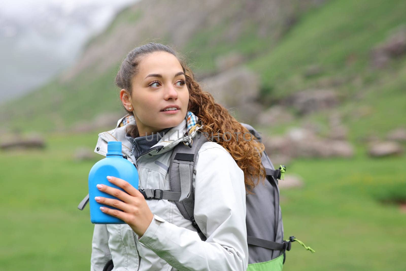 Hiker holding canteen looking at side standing in the mountain