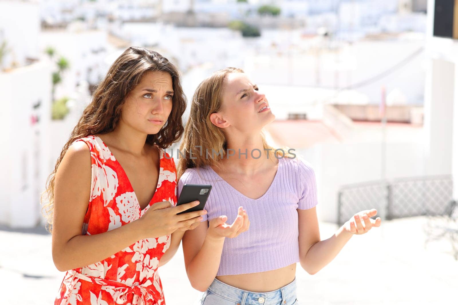 Lost tourists checking location on smart phone in a white town street on summer vacation