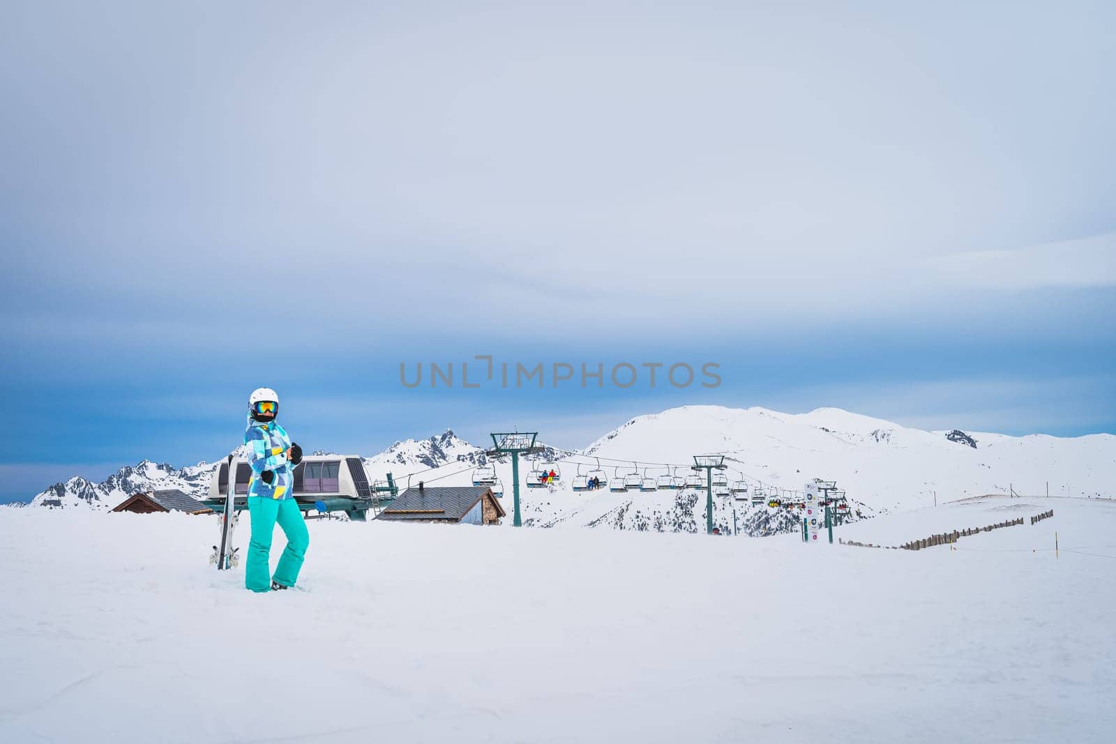 Portrait of a woman skier looking at a camera on the top of snowy Pyrenees Mountains with a ski lift in background. El Tarter, Grandvalira, Andorra