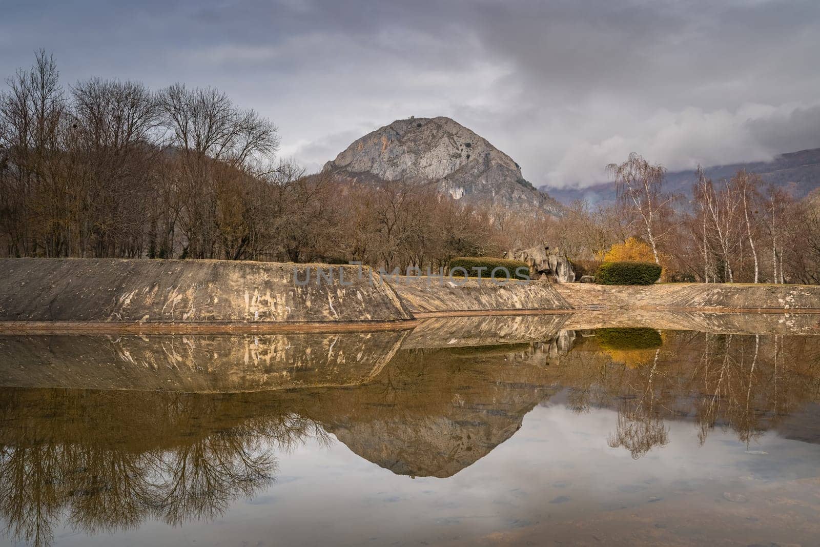Panorama with mountain peak and trees reflecting in artificial pond, Pyrenees Mountains, Tarascon sur Ariege, France
