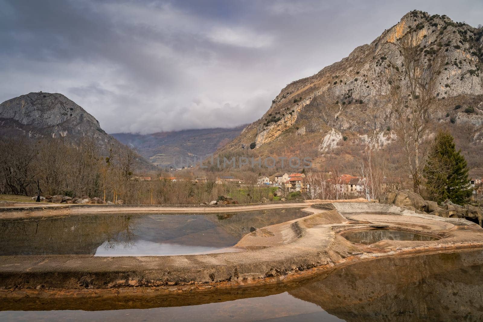 Mountains and trees reflecting in artificial ponds. Surba town hiding behind trees at the foothill of Pyrenees Mountains Tarascon sur Ariege France